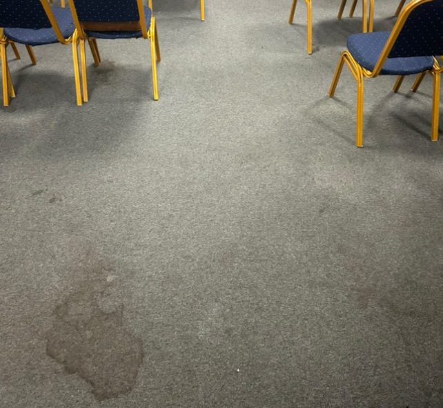 Tapis sale avec des taches, entouré de chaises en bois.