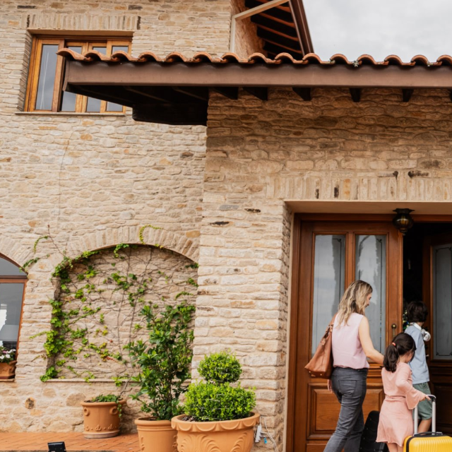 Femme et enfant s'approchant d'une maison en pierre avec des plantes.